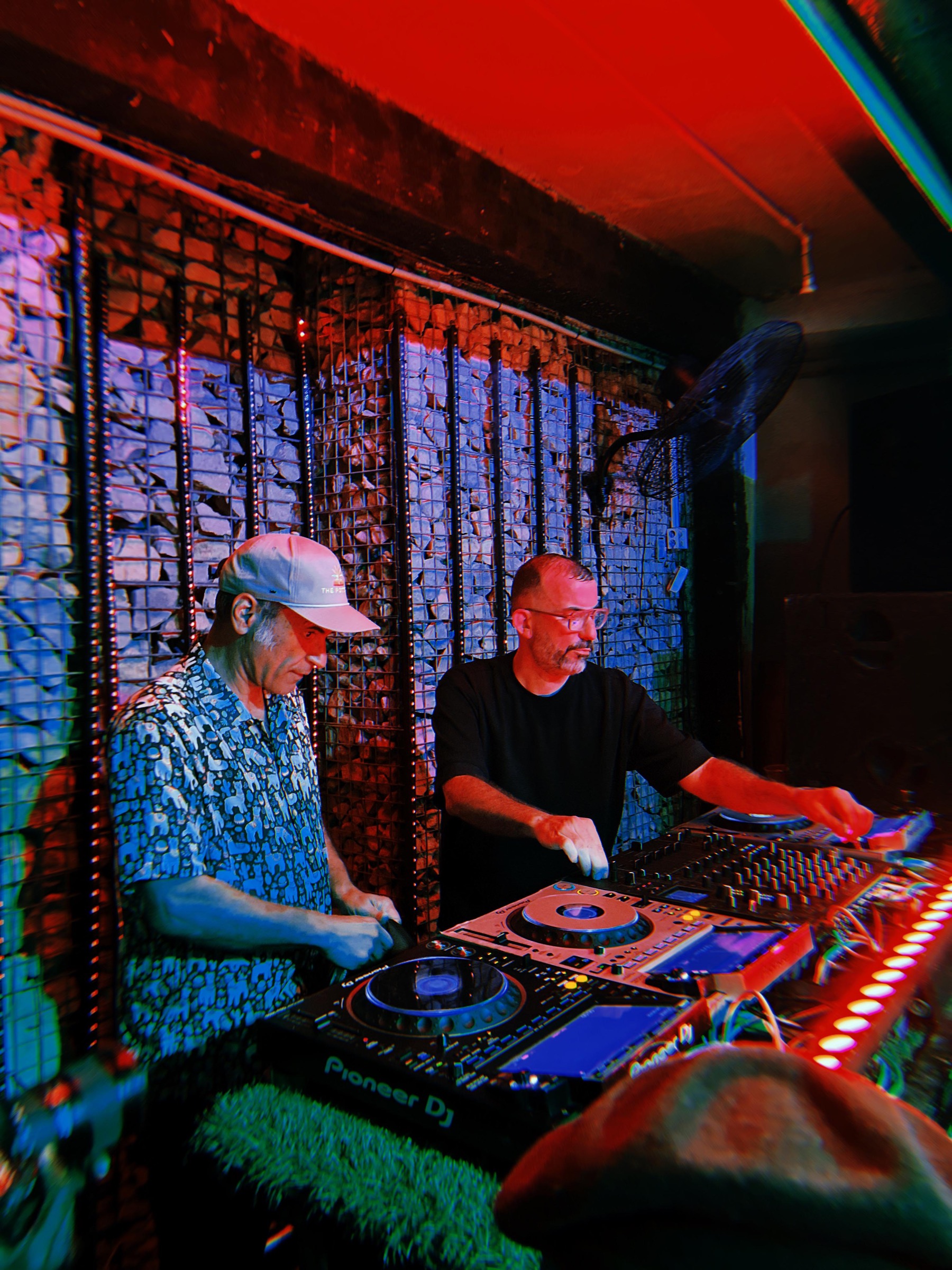 KULAS in a club booth with another artist under red and blue light.